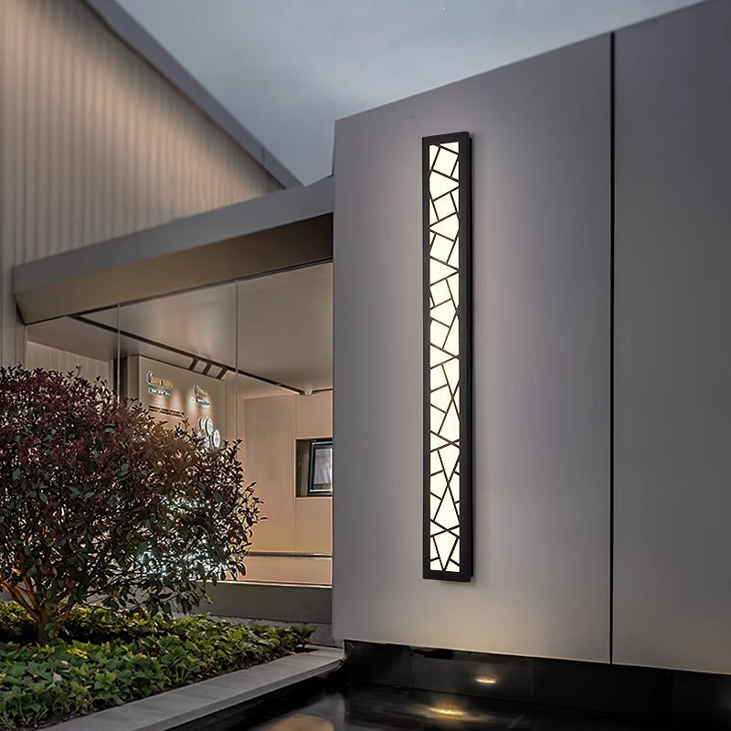 Lumière Outdoor Wall Light — textured outdoor wall light glowing warm on a dark exterior wall at dusk
